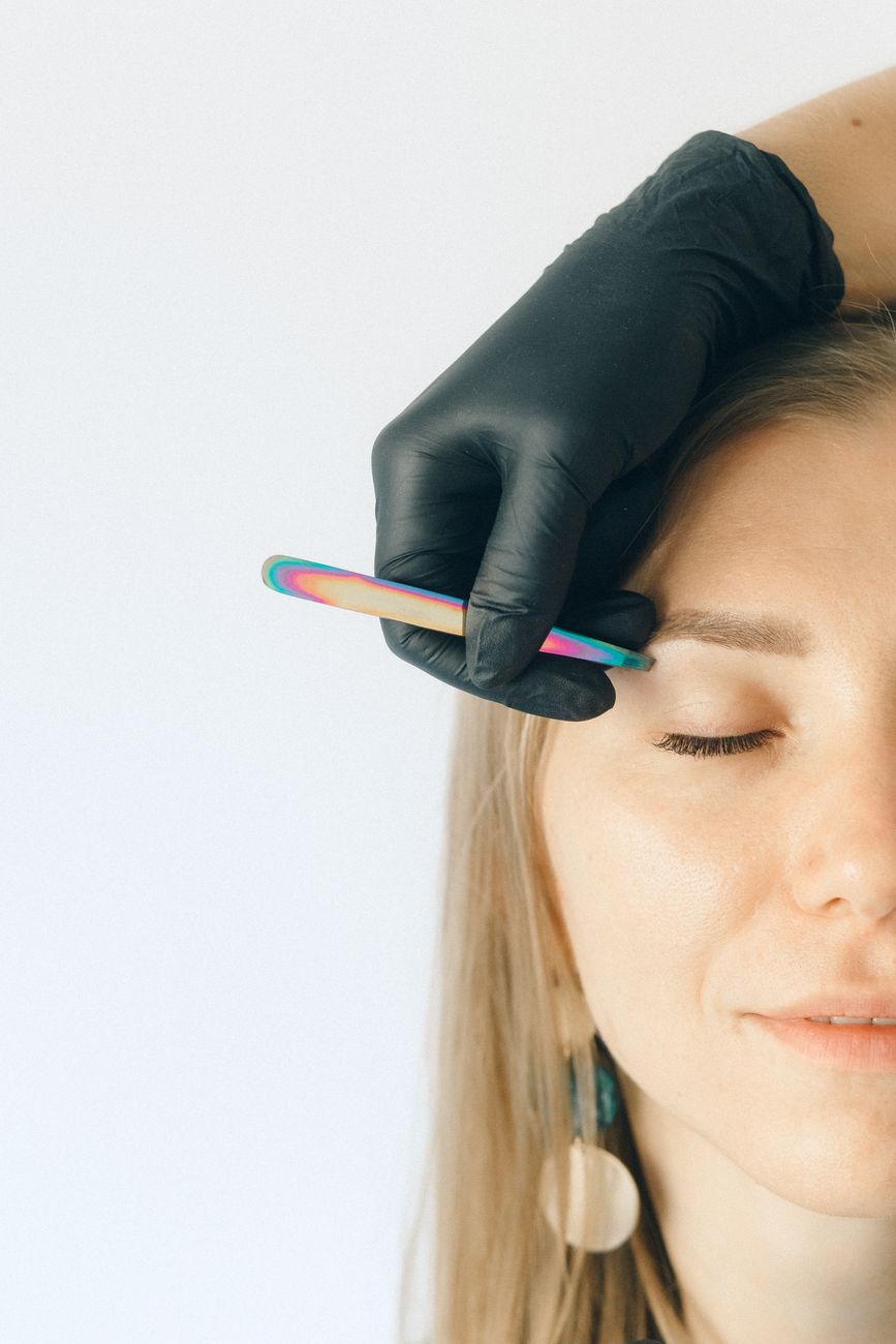 Close-up of a woman receiving an eyebrow plucking treatment with black gloves.
