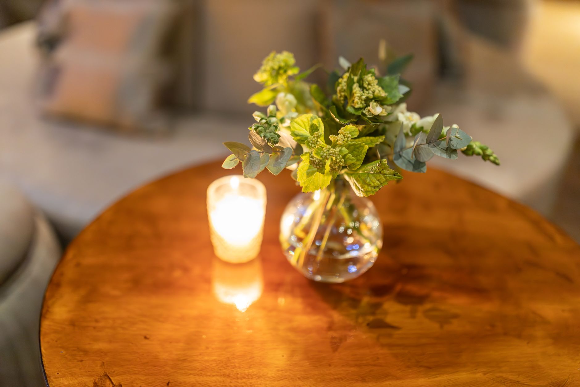 Cozy table setting with a lit candle and floral arrangement in a clear vase, perfect for interior design inspiration.